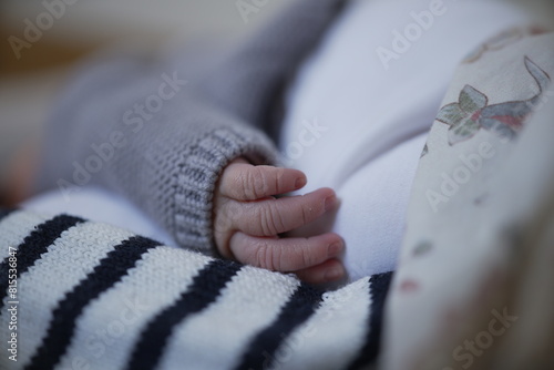 A close-up of a newborn baby's hand resting gently on a striped blanket. The baby is wearing a cozy gray sweater, highlighting the tenderness and delicate nature of newborn life, encapsulating 