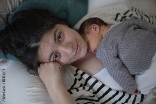 A tender scene of a mother and her newborn baby lying together, with the baby resting on the mother's chest. Both are relaxed and exhibit a strong bond, with the baby in a cozy gray 