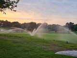 Water Sprinklers on a Golf Course at Sunset