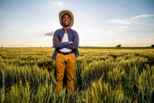 African farmer is standing in his growing wheat field. He is satisfied with progress of plants.