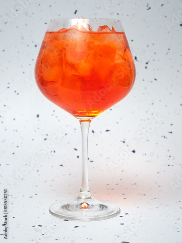 A close-up of a chilled Aperol Spritz filled with ice cubes. The vibrant orange drink stands out against a speckled background.    