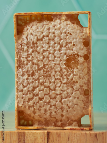 A close-up of a fresh honeycomb, showcasing its intricate hexagonal pattern and golden honey, set on a wooden surface with a blurred turquoise background