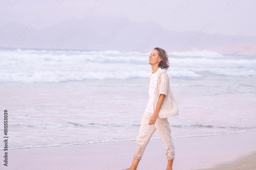 Peaceful stroll along the sandy beach at sunset for a young woman, with the gentle waves and soft pastel colors creating a tranquil atmosphere