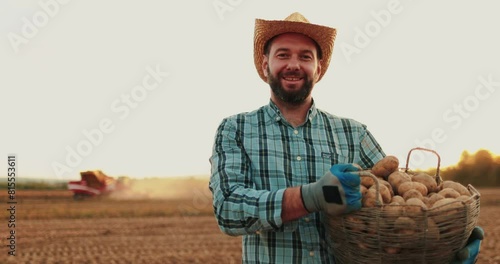 Portrait of a young man in a casual shirt and straw hat holding a box of potatoes on a farm. photo