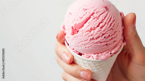Cono de helado blanco con bola de color rosa de fresa sujetado por una mano en primer plano. Postre de helado para verano photo