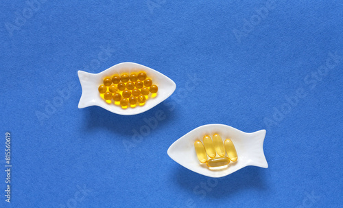 Dietary supplements or nutrition additions with fish oil, vitamin E and omega acids. Concept of preventing heart disease using fish oil. Flat lay of gelatin capsules on fish-shaped plates on blue 
