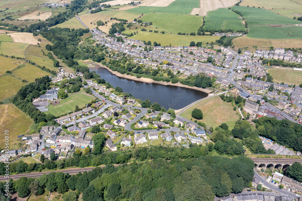 Obraz premium Aerial photo of the historic Yorkshire town of Huddersfield in the UK, showing the residential housing estates by a lake and train viaduct on a sunny day in the summer time