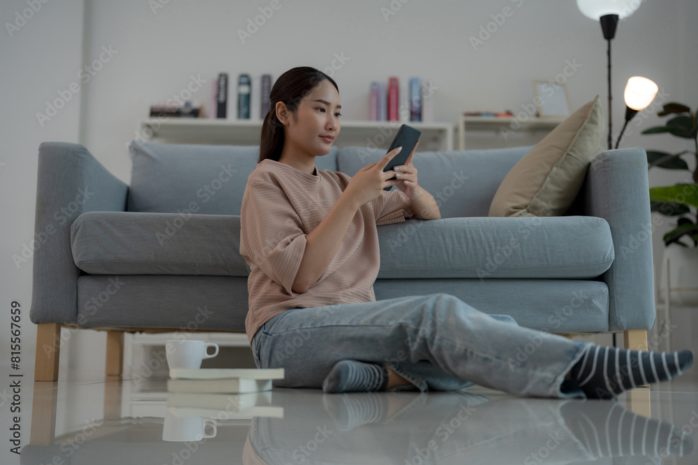 Obraz premium Young woman relaxing on floor at home with smartphone