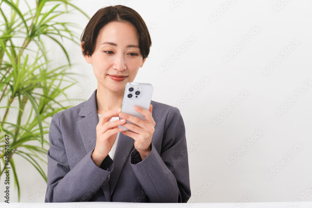 ビジネススーツを着てスマートフォンを操作している若い女性　ビジネスイメージ