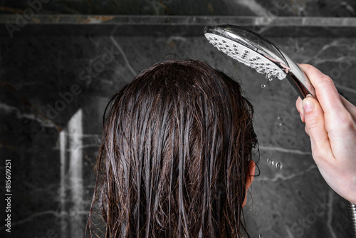 Young woman washing her hair by rinsing it under running water in the bathroom. © Natallia