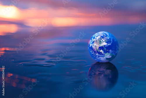 Small Earth globe on calm reflective water with a colorful sunset in the background creating a serene scene