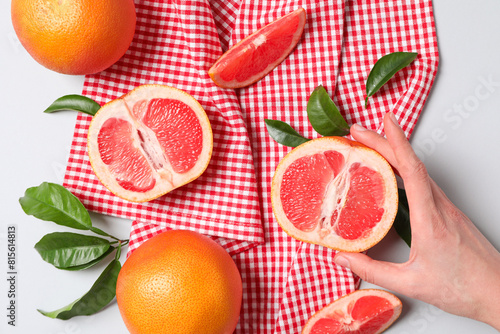 Whole and sliced grapefruits on towel and female hand on white background, top view