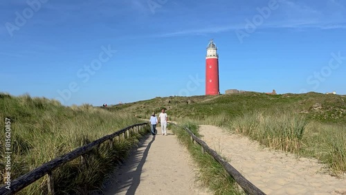 A diverse couple of caucasian men and an Asian women walking on a path to the lighthouse of Texel surrounded by dunes on a beautiful summer day in the Netherlands photo