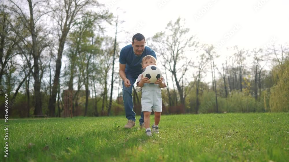 Baby toddler runs with a ball on the grass in the park. happy family kid dream concept. baby toddler son playing ball with father in summer park on grass outdoors. kid play ball lifestyle Baby toddler runs with a ball on the grass in the park. happy family kid dream concept. baby toddler son playing ball with father in summer park on grass outdoors. kid play ball lifestyle