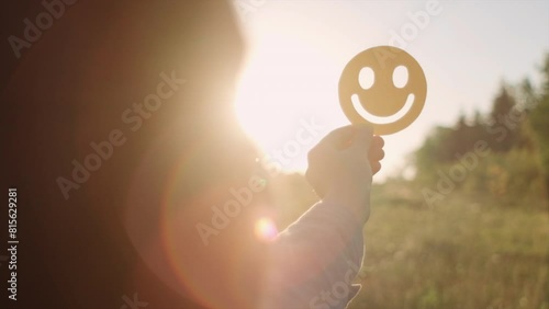Selective focus of woman holding yellow happy smile face on background amazing warm sunset or sunrise, good feedback rating and positive customer review, satisfaction survey, mental health assessment