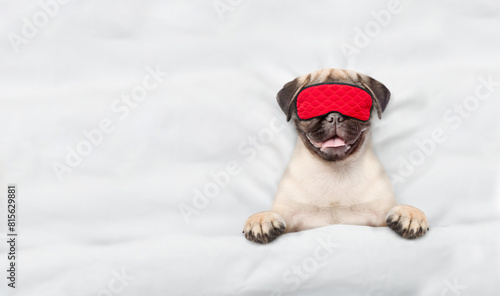 Cute Pug puppy wearing sleeping mask sleeps on a bed at home. Top down view. Empty space for text photo