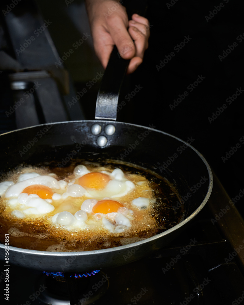 The cook prepares fried eggs in the kitchen. Low key concept of preparing delicious brunch with space for recipe or menu. The cook prepares fried eggs in the kitchen. Low key concept of preparing delicious brunch with space for recipe or menu.