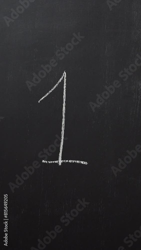 Hand writes the number 1 with white chalk on a black board. Vertical video