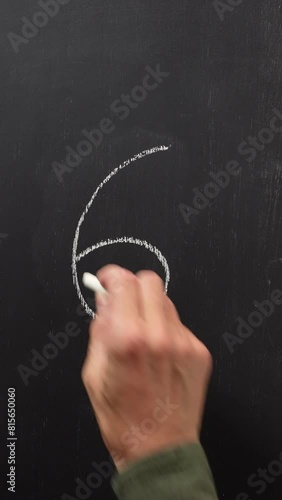 Hand writes the number 6 with white chalk on a black board. Vertical video