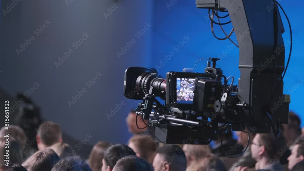 Videoed A professional video camera records a live event, focusing on the crowd ...