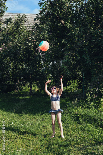 Child girl in a swimsuit plays with an inflatable ball. Childhood, leisure on weekends and holidays. Vertical