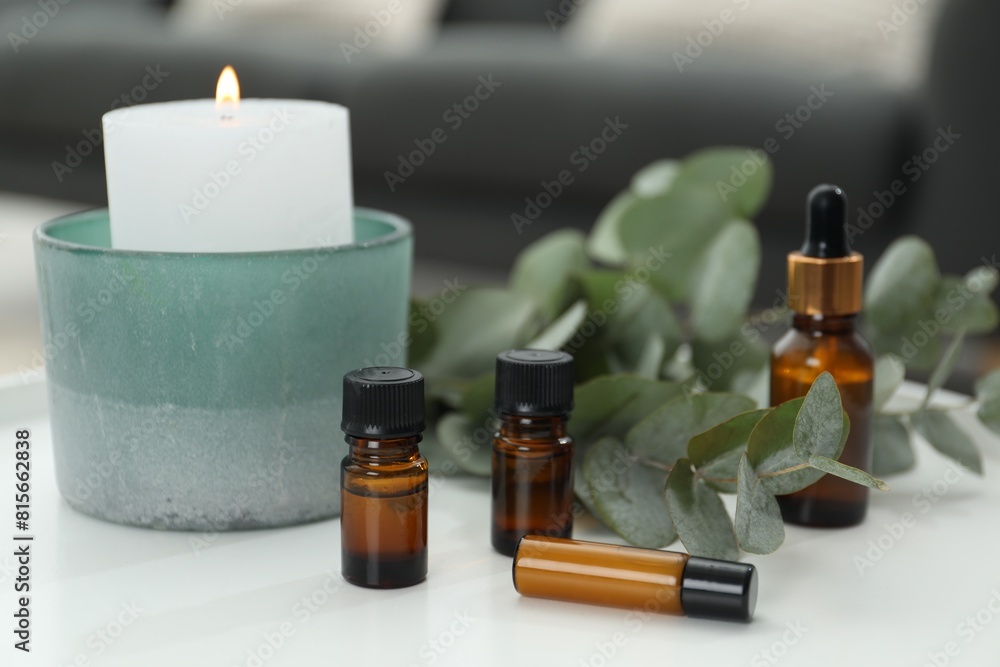Aromatherapy. Bottles of essential oil, burning candle and eucalyptus leaves on white table Aromatherapy. Bottles of essential oil, burning candle and eucalyptus leaves on white table