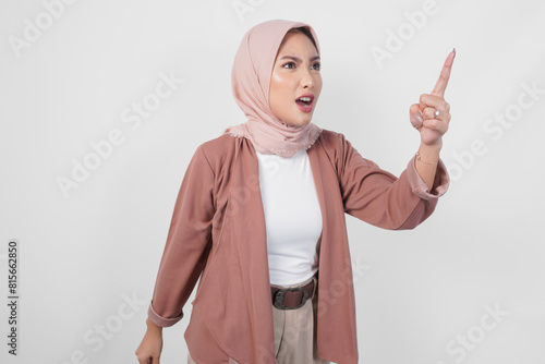 Billede på lærred Young Asian Muslim woman wearing hijab looking disgruntled irritated expression while pointing to camera, isolated by white background