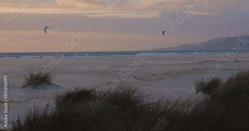 Man and child walking on the beach at sunset with kitesurfers kitesurfing with kite and board