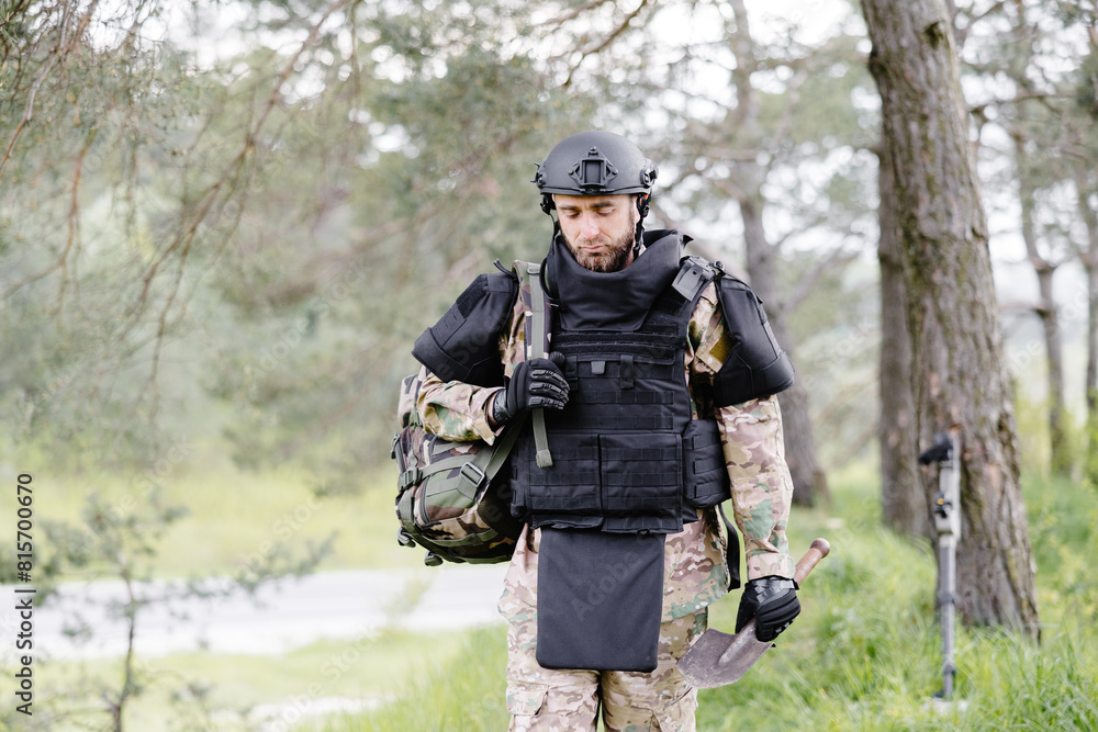 Young soldier in uniforms and tactical vest works in the forest and prepares for action at a temporary forest base. A man does in the work of demining the territory Young soldier in uniforms and tactical vest works in the forest and prepares for action at a temporary forest base. A man does in the work of demining the territory