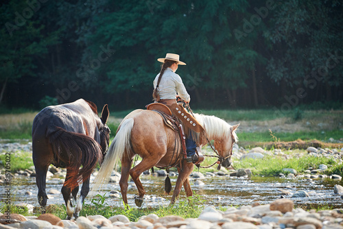 Cowgirl crossing the river riding a horse and leading a mule