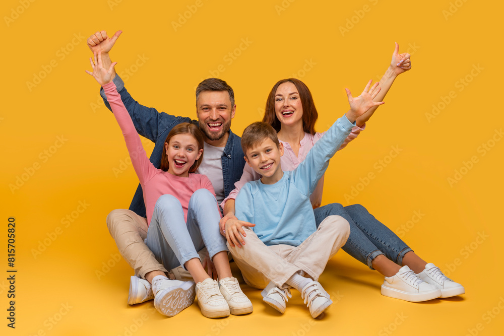 A joyful family sits closely together with arms raised in a celebratory gesture, smiling enthusiastically. A father and mother are behind their daughter and son, all sharing a moment of happiness A joyful family sits closely together with arms raised in a celebratory gesture, smiling enthusiastically. A father and mother are behind their daughter and son, all sharing a moment of happiness