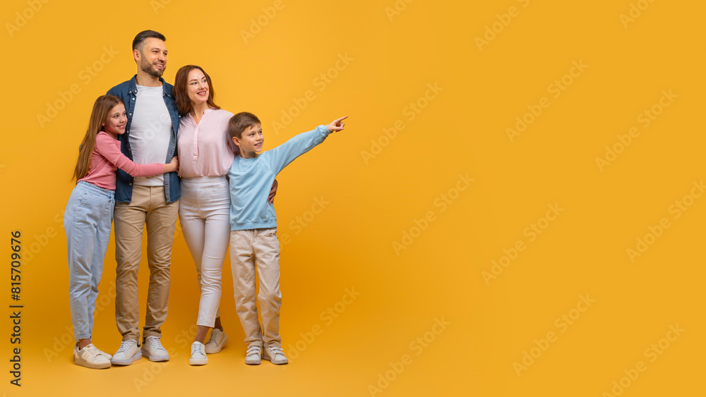 A happy family consisting of a father, mother, daughter, and son stand close to each other, with the son pointing excitedly to something off-camera, copy space A happy family consisting of a father, mother, daughter, and son stand close to each other, with the son pointing excitedly to something off-camera, copy space