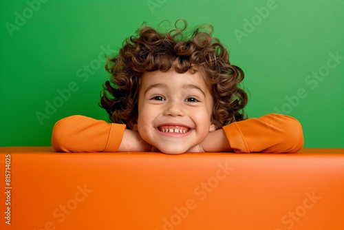 Happy child peering over orange surface