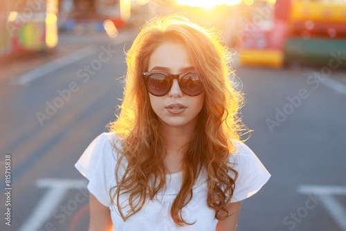 Beautiful summer urban portrait of a beautiful fresh red-haired woman with red hair with fashion sunglasses in a white T-shirt on the street at sunset