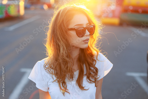 Cool beautiful redhead young woman model with stylish sunglasses in a white t-shirt on a summer day at sunset