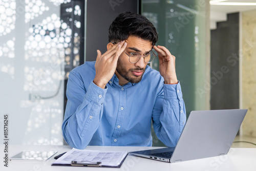 Stressed businessman working on a laptop and holding head in hands in modern office