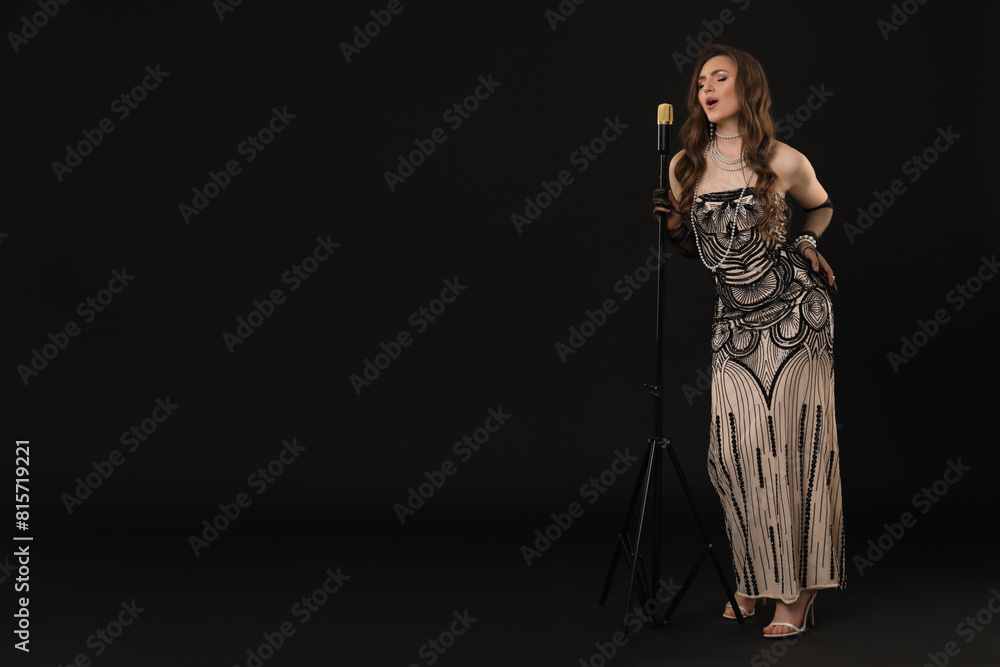 Beautiful young woman in stylish dress with microphone singing on black background, space for text Beautiful young woman in stylish dress with microphone singing on black background, space for text