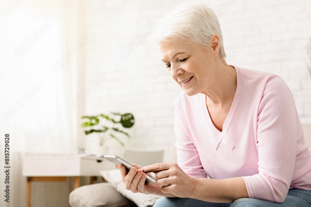 Elderly woman is seated on a couch indoors, engrossed in her cell phone. She appears focused as she interacts with the device, possibly messaging or scrolling through content. Elderly woman is seated on a couch indoors, engrossed in her cell phone. She appears focused as she interacts with the device, possibly messaging or scrolling through content.