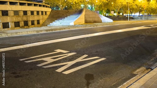 Urban night scene with a taxi sign on the asphalt and two cars passing by. One belongs to the Bolt company. Exclusive lane for taxis