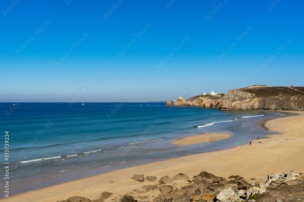La plage de Pen Hat et la pointe du Toulinguet se dessinent sous un ciel bleu, tandis que les eaux turquoises de la mer d'Iroise se parent d'écume blanche, offrant un spectacle maritime enchanteur.
