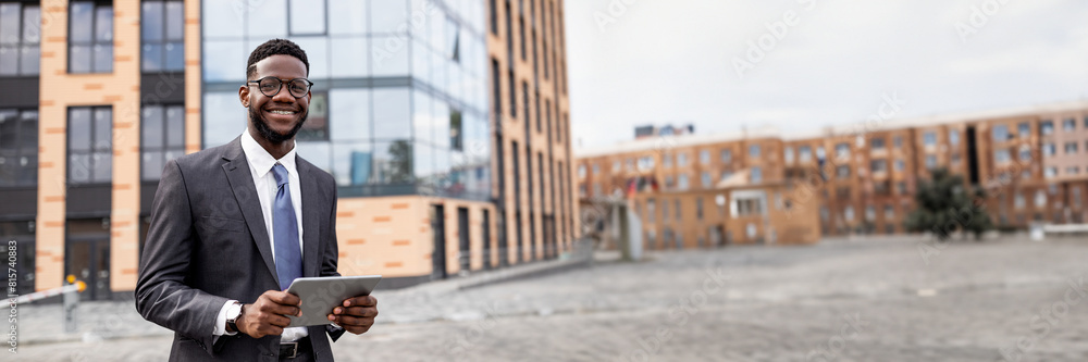 Business news. Happy black businessman using digital tablet walking outdoors near modern office building in urban area cityscape, smiling to camera, copy space, web-banner Business news. Happy black businessman using digital tablet walking outdoors near modern office building in urban area cityscape, smiling to camera, copy space, web-banner