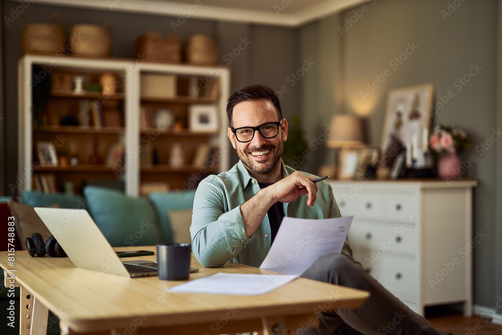 A portrait of a happy male financial advisor holding a report in his hand and sitting in front of a laptop A portrait of a happy male financial advisor holding a report in his hand and sitting in front of a laptop