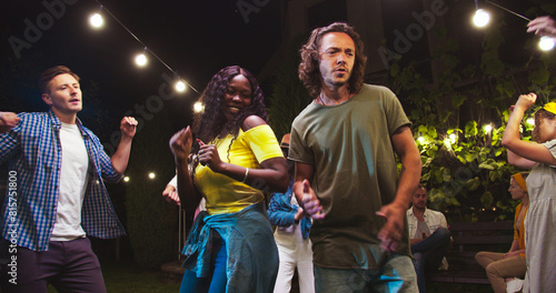 Happy African American girl and Caucasian boy having fun and dancing outdoor. Joyful mixed-races young friends moving to music at party in garden. Beautiful female in hat dances. Party concept