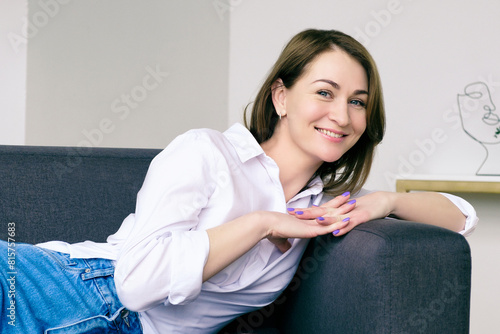 young smiling woman in blue jeans and a white shirt is sitting on the sofa