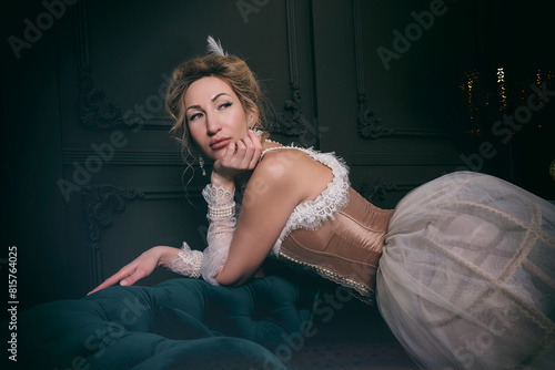 a young woman in an 18th century dress and lace in a boudoir is sitting in an armchair in a sexy and sensual way photo