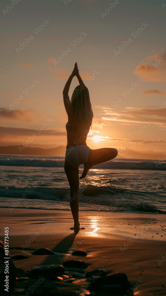 A young woman practicing yoga on the sandy beach as the sun sets in the background, casting a warm glow over the scene. She performs various yoga poses.