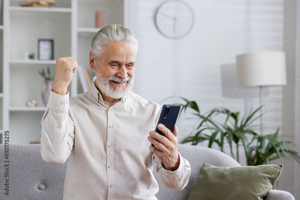Excited senior man celebrating success while using smartphone at home Excited senior man celebrating success while using smartphone at home