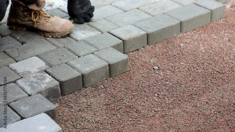 Worker Laying Paving Stones, Close-up of a worker's hands laying gray paving stones on a street, wearing gloves.
