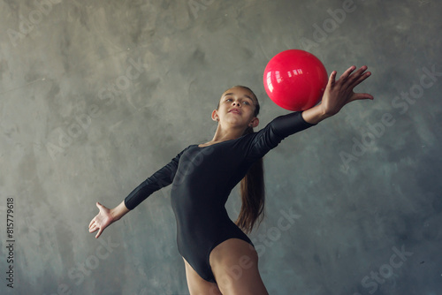 a young girl rhythmic gymnastics in a black bodysuit performs exercises with a ball