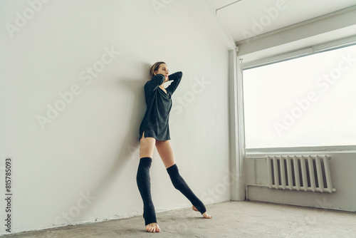 ballerina standing against the wall in a half-skirt and knee socks and looking out the window